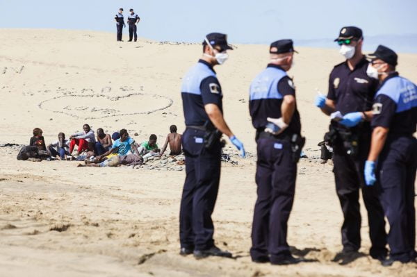 Would-be immigrants rest on Maspalomas beach next to policemen, on Gran Canaria in Spain's Canary Islands