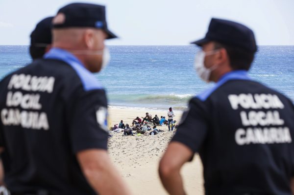 Would-be immigrants rest on Maspalomas beach next to policemen, on Gran Canaria in Spain's Canary Islands