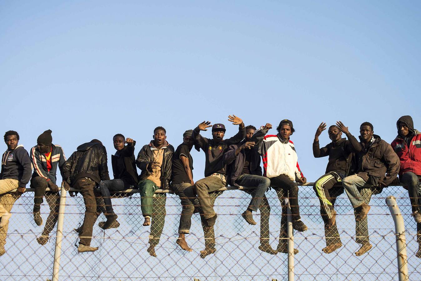 African migrants sit atop a border fence between Morocco and Melilla