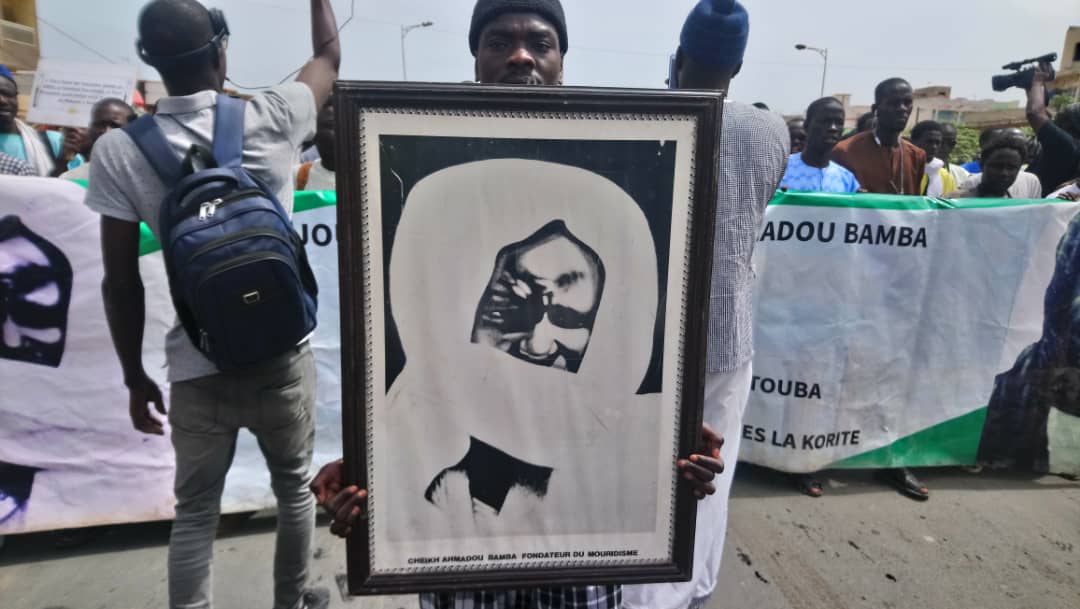  - Un groupe de personnes regardant un homme faisant un tour sur une planche à roulettes - Amadou Bamba